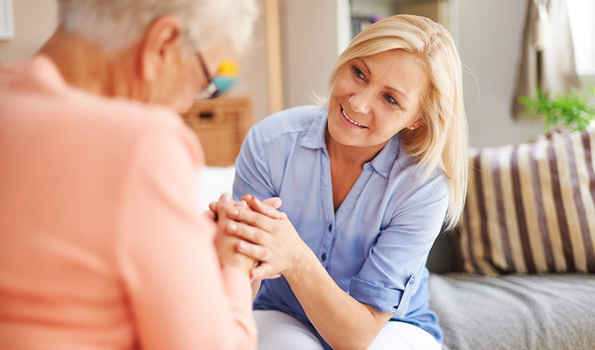 A woman caregiver holding hands with a senior woman.