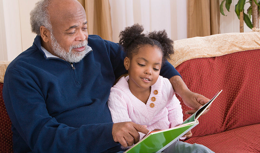 A senior man reading to a little girl.