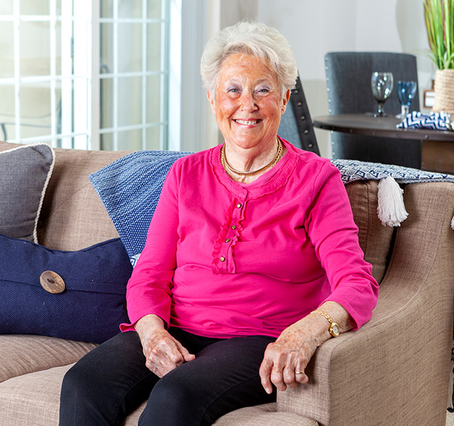 Happy resident sitting on a couch with a pretty pink blouse on.