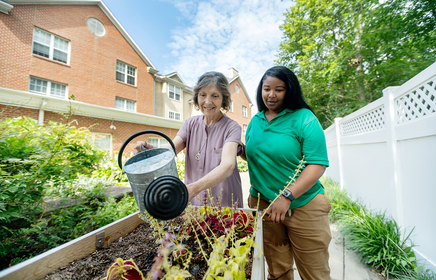A resident watering plants with a caregiver.