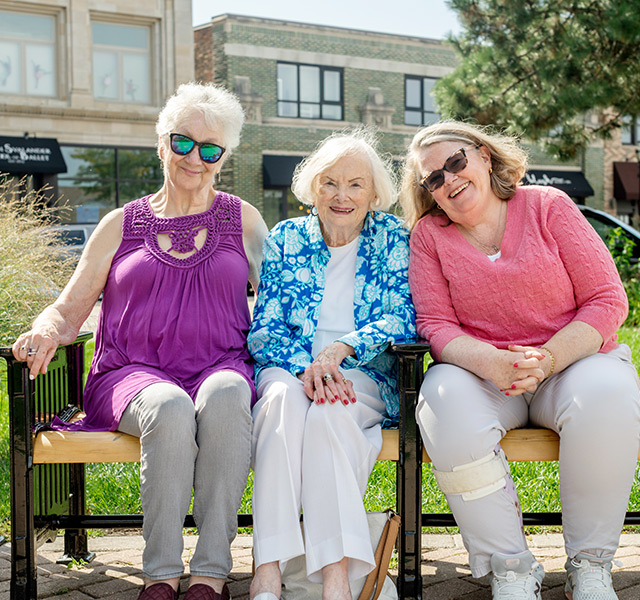 Three residents sitting on a bench in the sun.