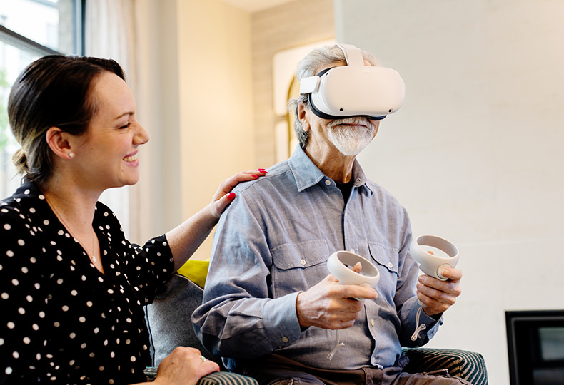 A resident playing with a VR headset and a caregiver near by.