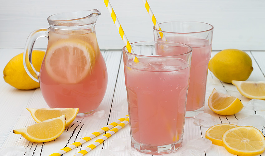 Two glasses of pink lemonade, a pitcher and some lemons.