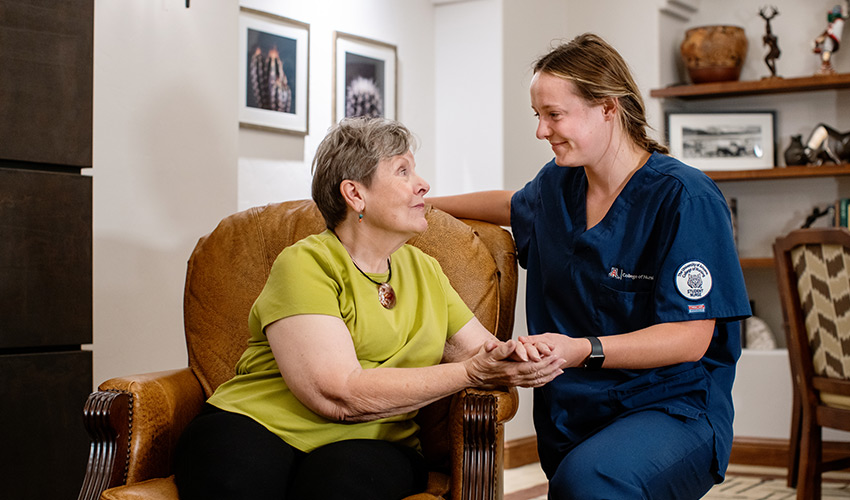 A nursing student kneeling next to a woman resident in a chair.