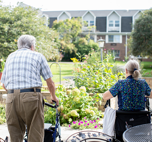 Two residents are using a walker and a wheelchair outside.