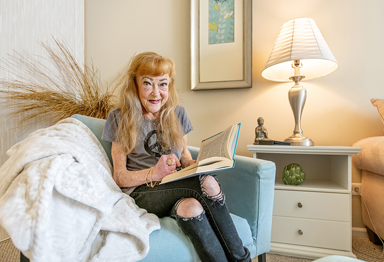A resident is sitting in a chair and holding a book.