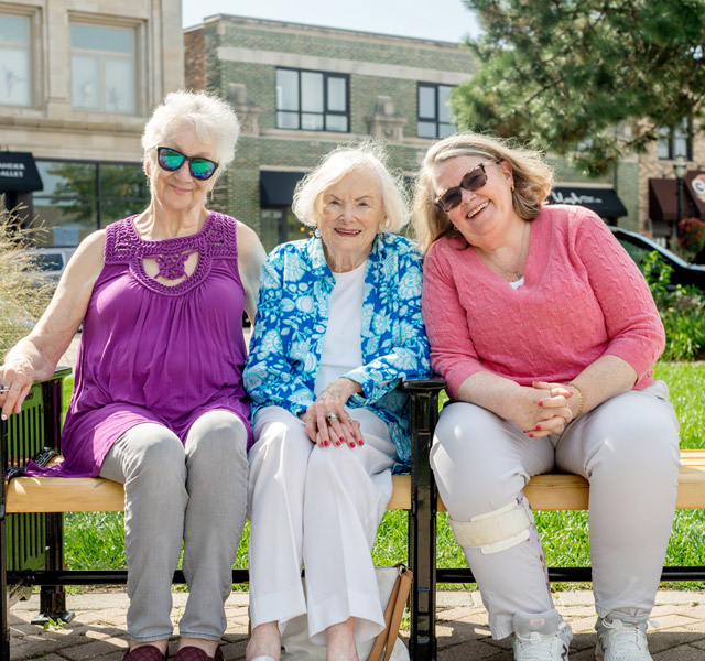 Three residents are sitting outside on a bench.