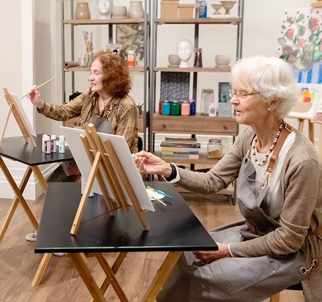 Two residents are painting on canvases in an art class.