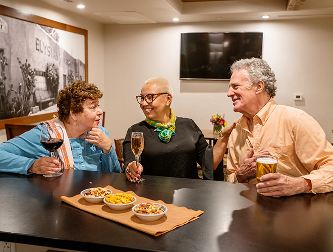 Three residents are sitting together, drinking wine and having a snack at the bar.