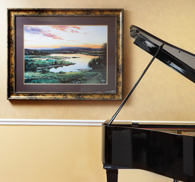 Black grand piano right by art on the wall.