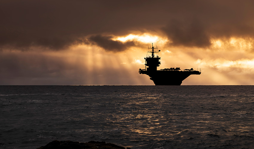 A navy ship in the ocean at sunset.