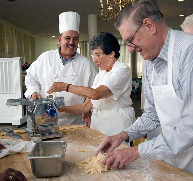 couple at a pasta making class with the chef smiling and teaching