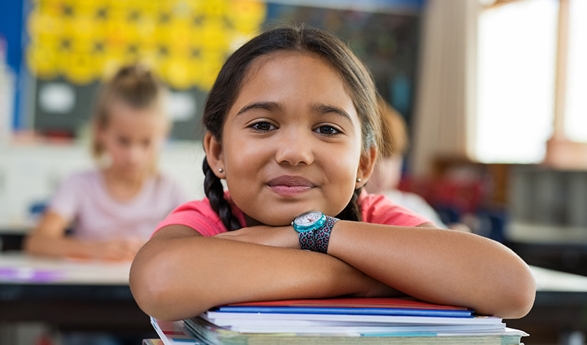 A young girl resting her head on her arms on her books.