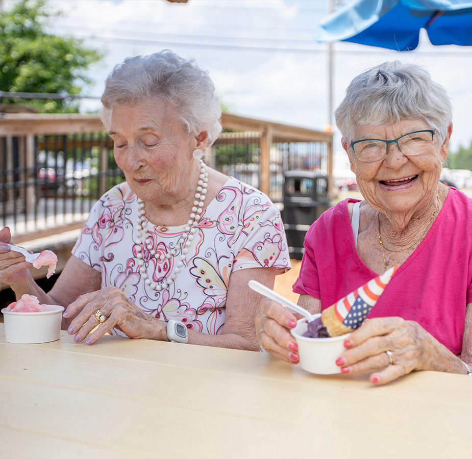 Two residents are sitting outside eating ice cream together.