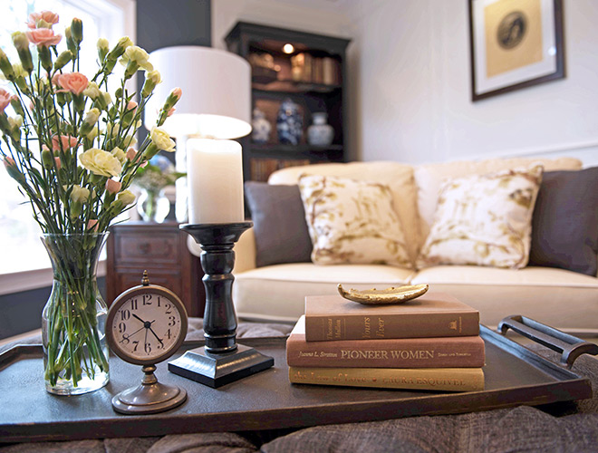 Furnished living room with a couch and coffee table featuring a vase of flowers, some books, and a clock.