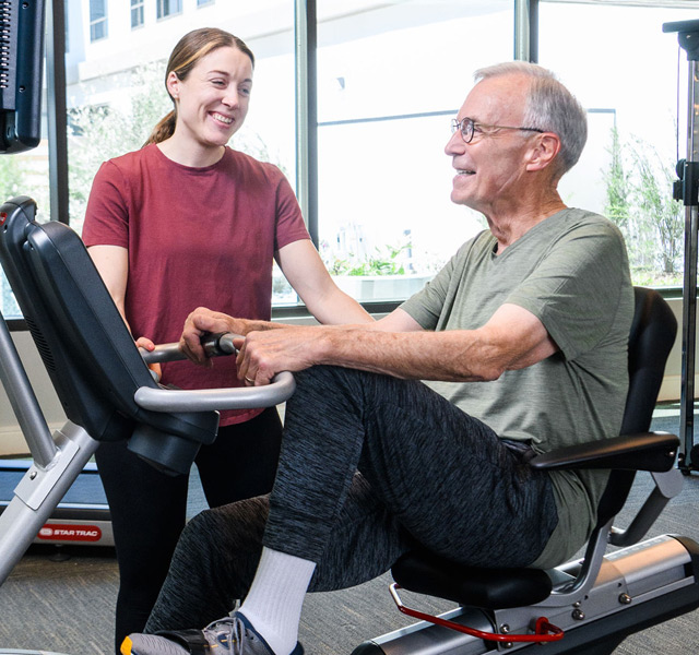 Resident uses fitness machine with trainer.