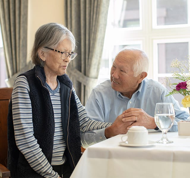 The Fountains at Albemarle Assisted Living A happy couple holding hands while enjoying a meal together.