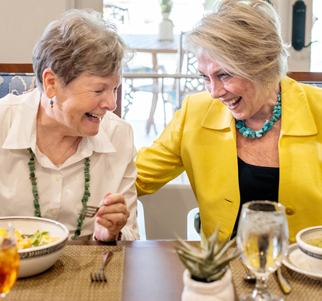 Female residents share a laugh while they eat and drink wine.