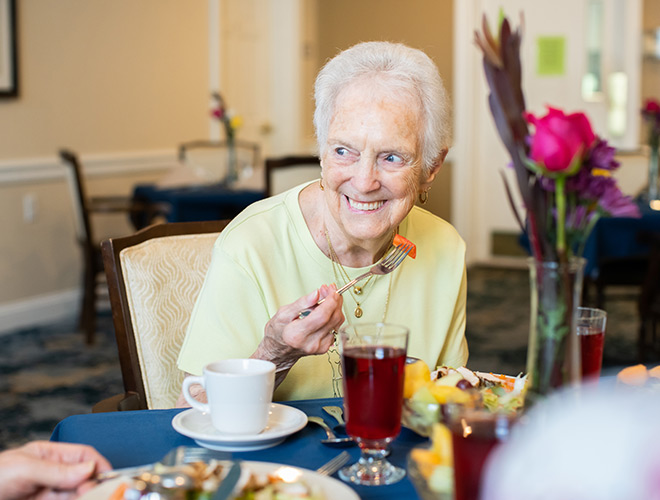 A resident smiling and eating at the dinner table