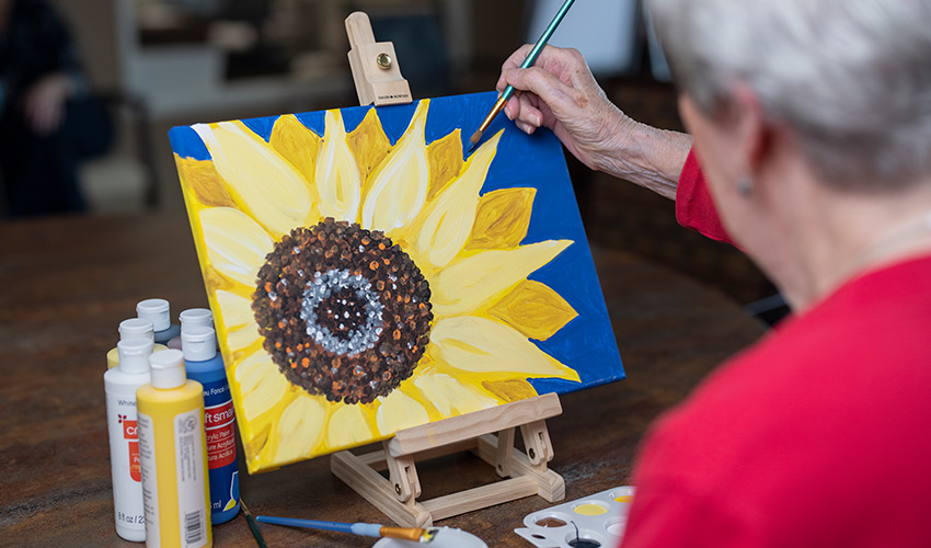 A senior woman painting a sunflower.