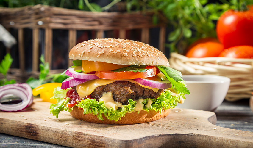 A hamburger topped with lettuce, cheese, tomato and red onion.