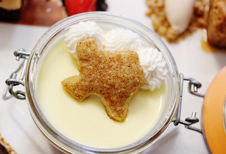 A custard dessert in a jar with a cookie and whipped cream on top.