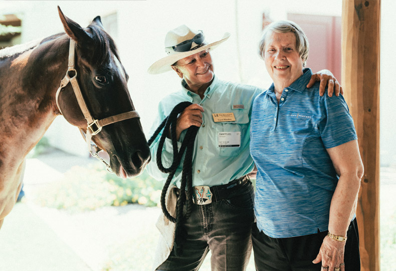 An associate with their arm around a smiling resident with a horse.