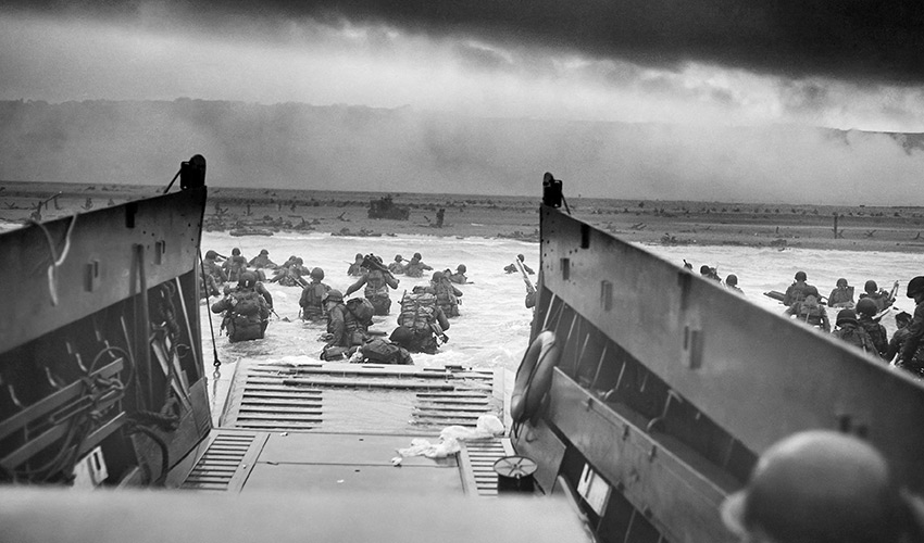 Vintage World War II photo of American troops wading ashore on Omaha Beach during the D-Day invasion.