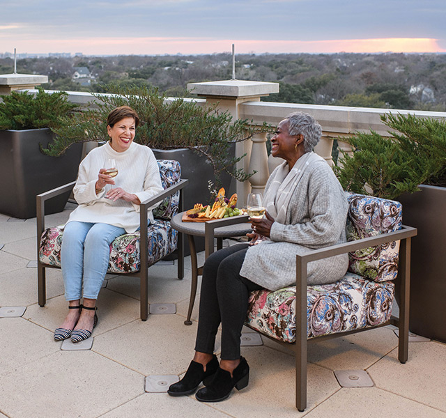 two residents enjoying wine and a charcuterie board outside on a large balcony area