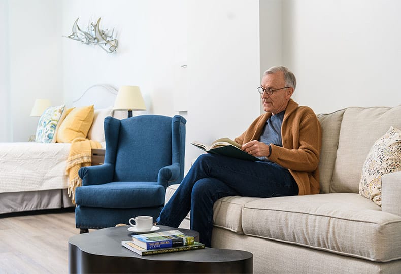 A resident sitting on a sofa reading a book.