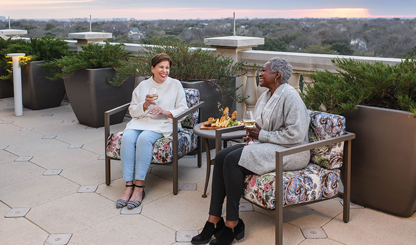 Two women sitting on the rooftop having drinks.