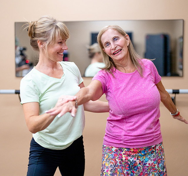 A resident is being assisted by a caregiver during a fitness class.