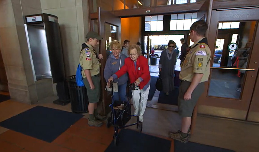Boy scouts helping people through a doorway.