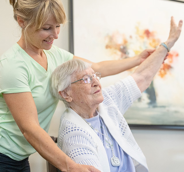A resident is stretching with assistance from a caregiver.