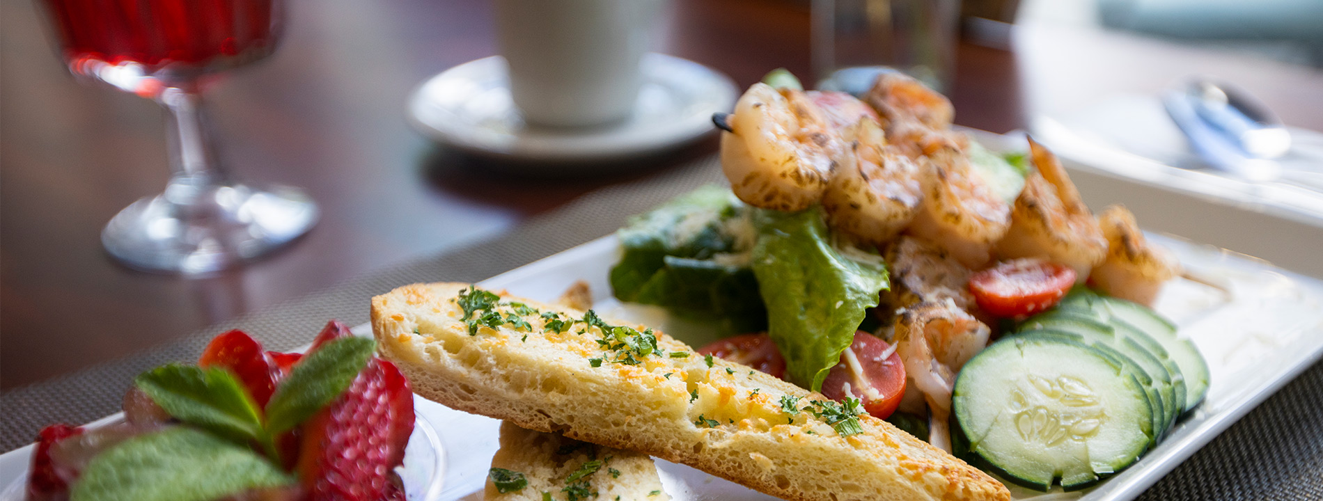 close up of a plate of food consisting of fruit, bread and a salad with grilled shrimp on top