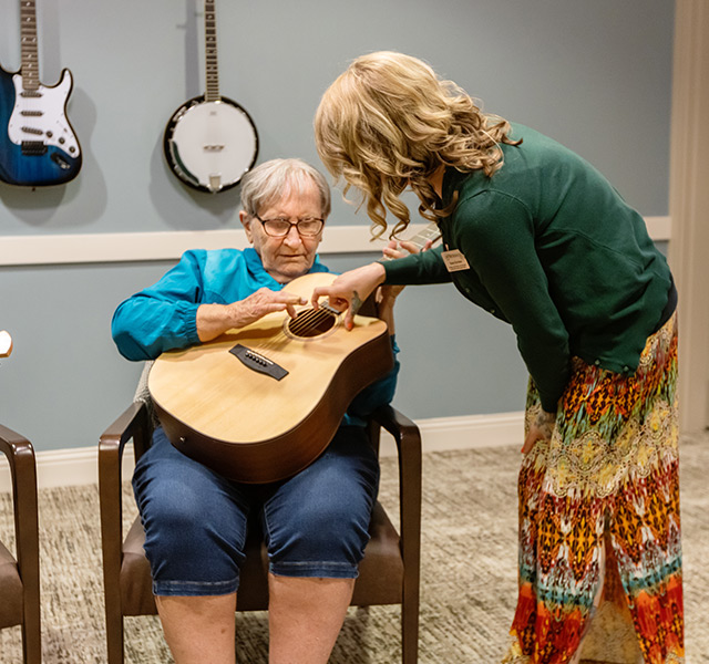 A person helping a resident play the guitar.
