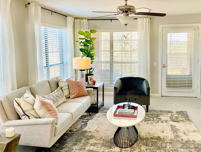 Furnished living room space wtih sofa and table and chair with windows.