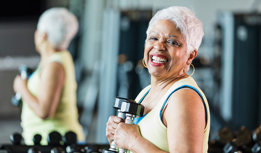 A senior woman holding a set of hand weights in the gym.