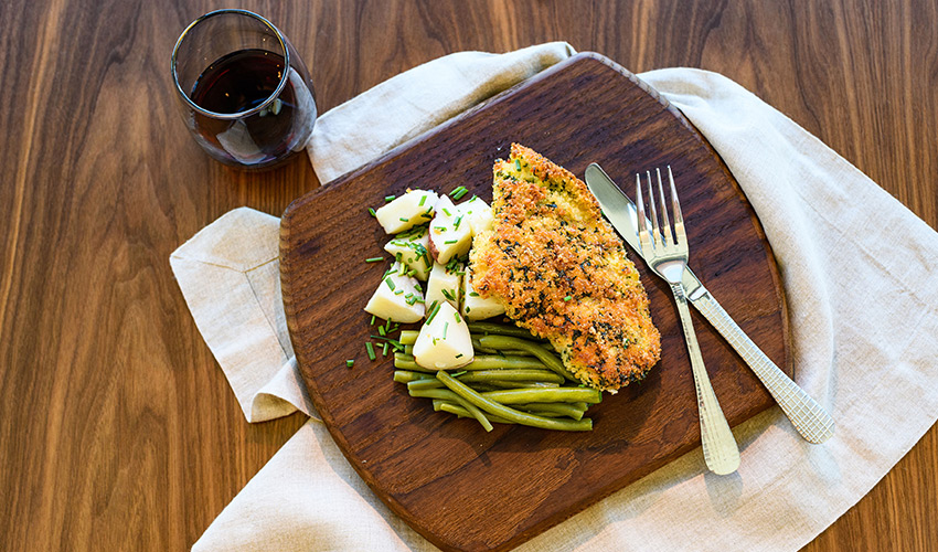 A plate of breaded fish with potatoes and green beans.