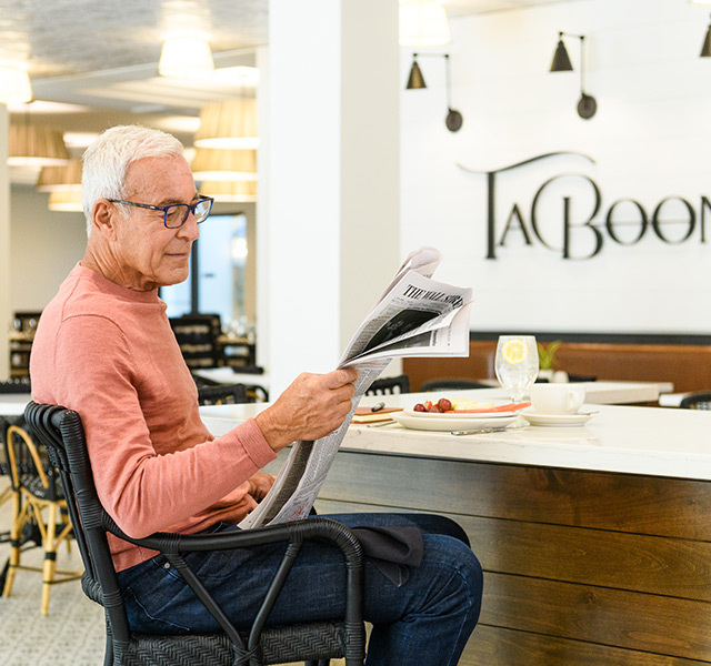 A resident is reading the newspaper in the cafe at The Watermark at Napa Valley.