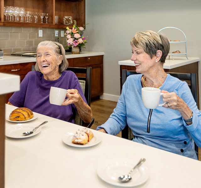 Two residents are holding coffee cups with plates of pasties in front of them.
