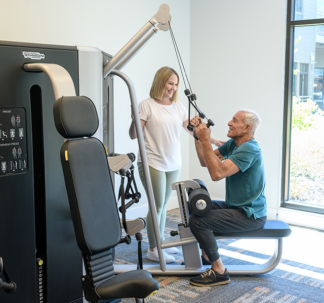 A resident using a fitness machine with the guidance from a team member.
