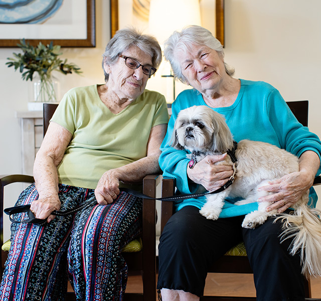 Two residents are sitting next to each other and holding a small dog.