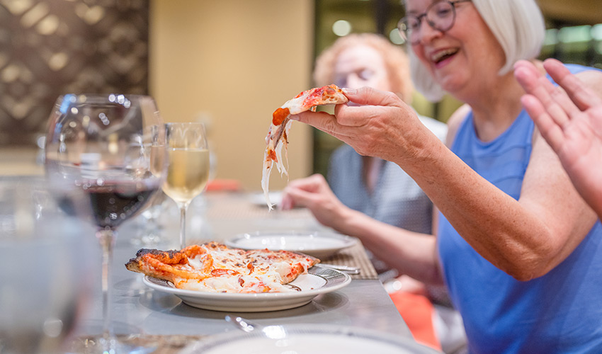 A senior woman eating a slice of pizza.