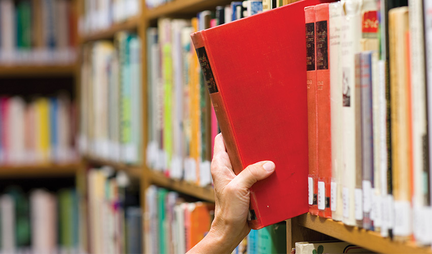 person grabbing a book from a shelf in a library