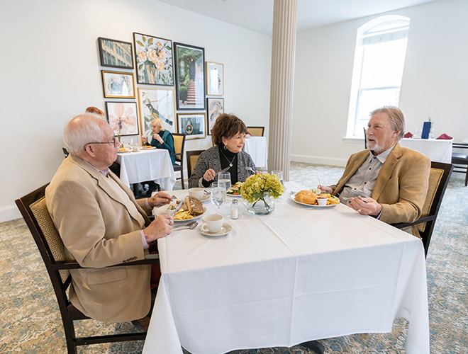 Three residents are having a meal together in the dining area at Woodbury Mews.