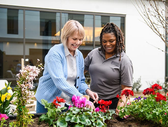 A resident and a personal ambassador program member working in an outdoor garden found on-site at a Watermark Retirement Community Property