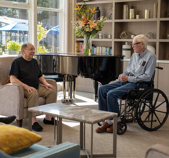 Residents enjoying a chat in a seating area by a piano.