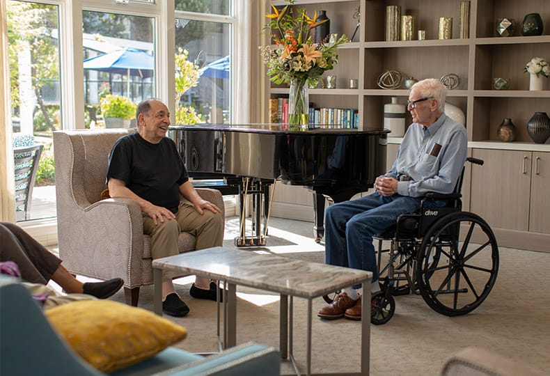 Residents enjoying a chat in a seating area by a piano.