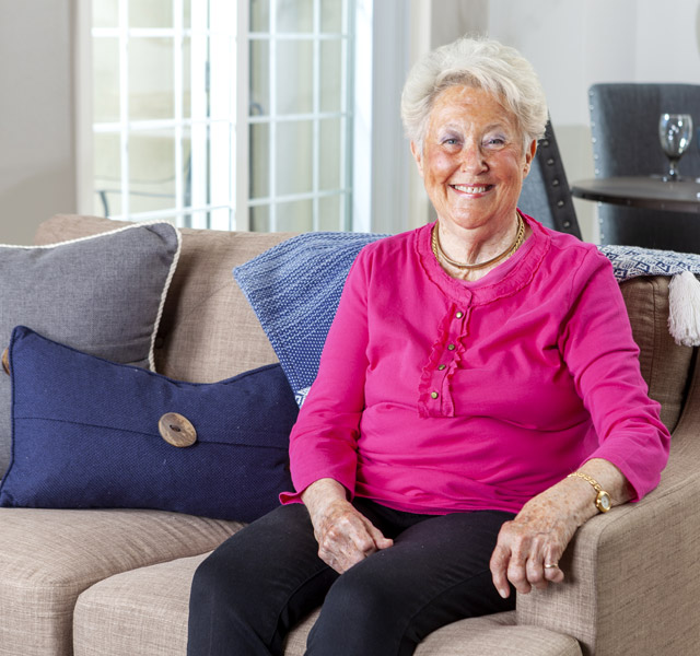 A smiling resident sitting on a couch wearing a pink shirt.